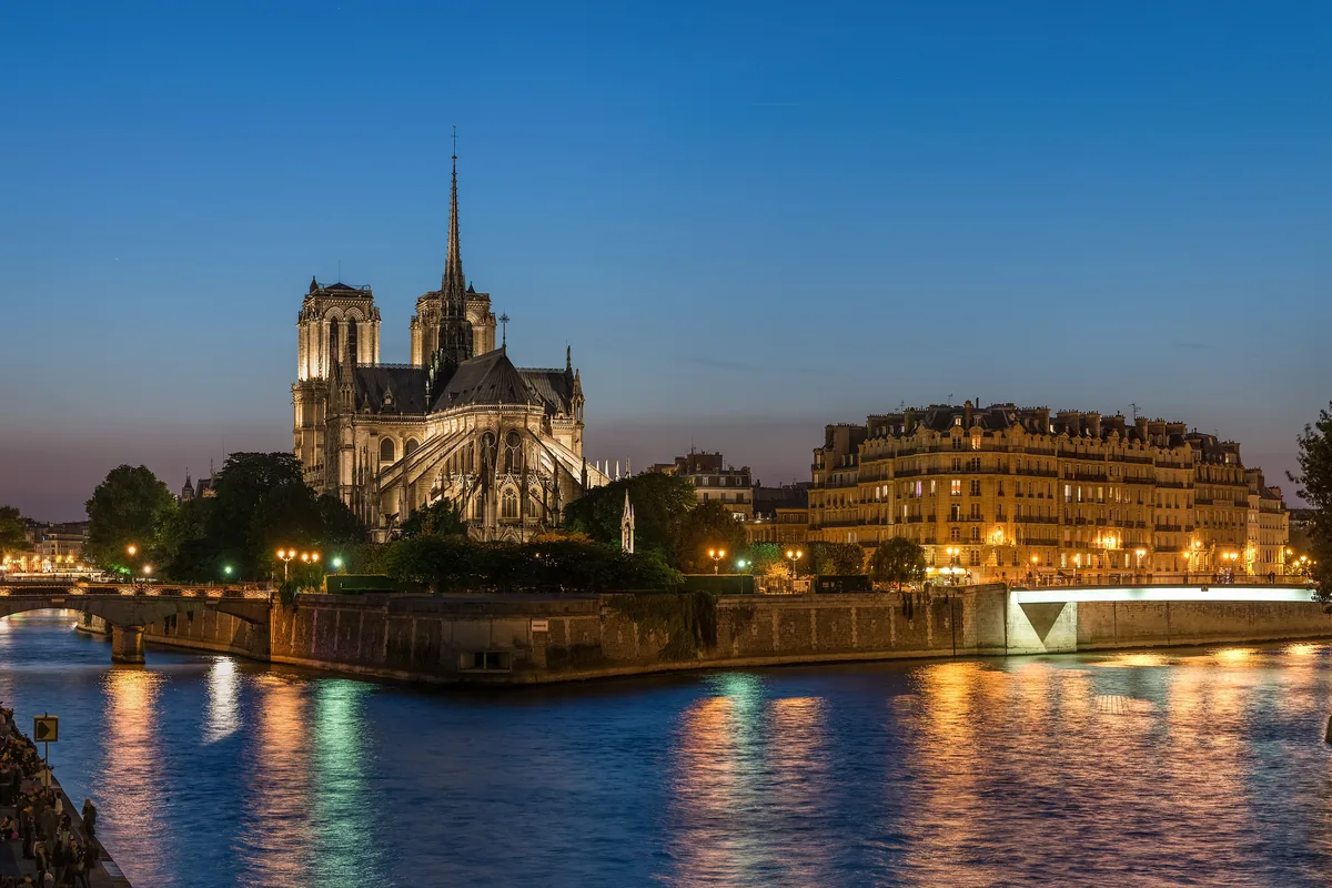 Notre-Dame and the Île de la Cité lit up at dusk, seen from the Seine